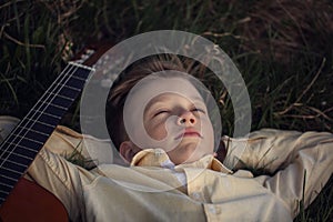 Cute boy lies on the grass with a guitar on sunset