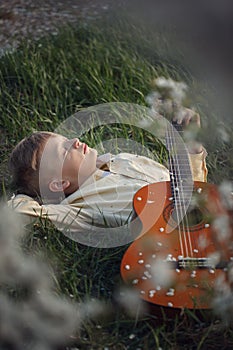 Cute boy lies on the grass with a guitar on sunset