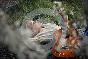 Cute boy lies on the grass with a guitar on sunset