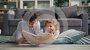 Cute boy listening to fairy-tale while his mother reading book lying on floor