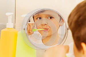 Cute boy looking in the glass and brushing teeth