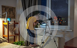 Cute boy is looking through a telescope at the night starry sky. Children`s passion for space exploration