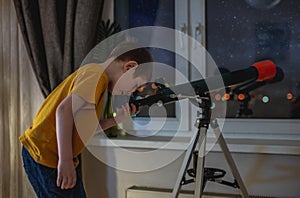 Cute boy is looking through a telescope at the night starry sky. Children`s passion for space exploration
