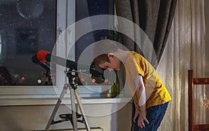 Cute boy is looking through a telescope at the night starry sky. Children`s passion for space exploration