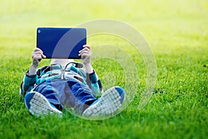 Cute boy lying in park and using tablet pc