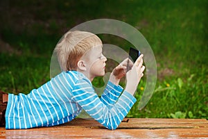 Cute boy lying in park and using tablet pc