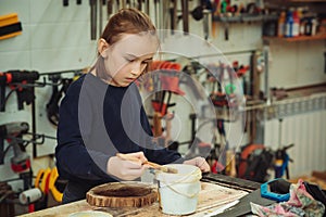 Cute boy makes wooden clock in the workshop. Young carpenter working with wood in craft workshop