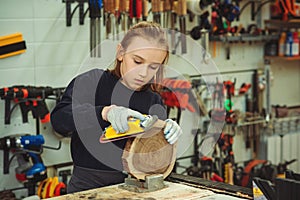 Cute boy makes wooden clock in the workshop. Young carpenter working with wood and sandpaper in craft workshop