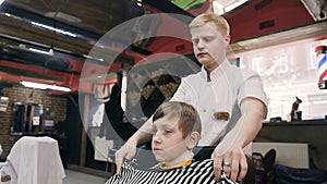 Cute boy in the men`s hairdressing salon. The hairdresser cuts her hair to a little client. New hairstyle. The boy in