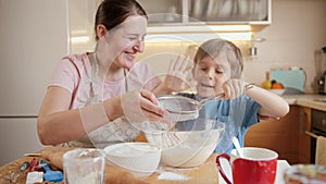 Cute boy with mother sifting flour with sieve for cake or pie dough. Children cooking with parents, little chef, family