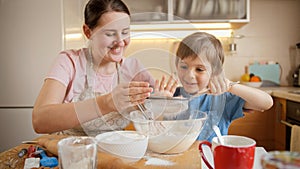 Cute boy with mother sifting flour with sieve for cake or pie dough. Children cooking with parents, little chef, family