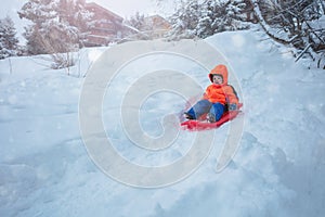 Cute boy in orange ski sport outfit go downhill on the sledge