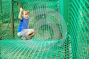 Cute boy overcomes obstacles in rope adventure park. Summer holidays concept. Happy kid playing at rope adventure park. Amusement