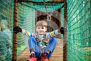 Cute boy overcomes obstacles in rope adventure park. Summer holidays concept. Happy kid playing at rope adventure park. Amusement