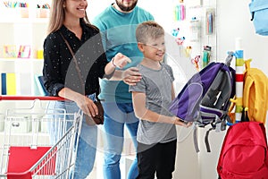 Cute boy with parents choosing backpack