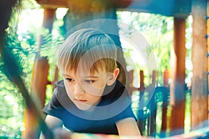 Cute boy passing cable tunnel. Outdoors playground, leisure for kids. Adventure rope park