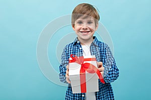 Cute boy in a plaid shirt holds out his lover`s gift on a light blue background with copy space