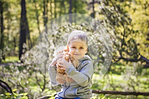 A cute boy is playing with a bear cub in the forest. The sun`s rays envelop the space of the clearing with a stump. A magical