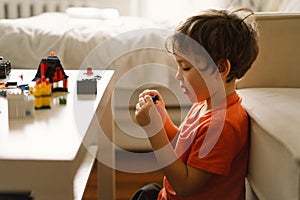 Cute boy is playing constructor at home. Kid playing block toys in home at nursery.