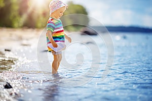 Cute boy playing with paper boat on the seashore.