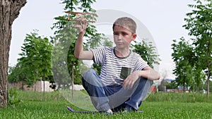 A cute boy is playing in the park with a toy airplane depicting the flight of an airplane. A happy child is sitting on