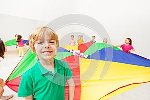 Cute boy playing rainbow parachute with friends