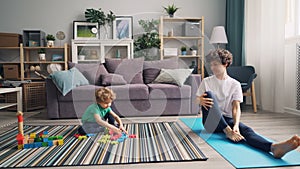 Cute boy playing with toys on floor while cheerful mother doing yoga on mat