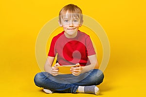 Cute boy playing video games on smartphone. Kid sitting on floor. Happy boy smiling. Child wears red tshirt