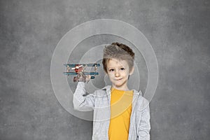 Cute boy playing with wooden airplane toy flying over the gray wall at home. Happiness and freedom