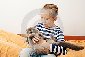 Cute boy plays with a cat at home. Happy kid hugging his cat