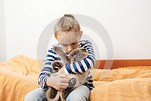 Cute boy plays with a cat at home. Happy kid hugging his cat