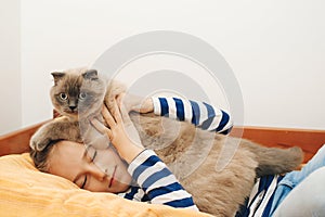 Cute boy plays with a cat at home. Happy kid hugging his cat