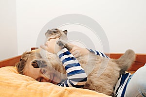 Cute boy plays with a cat at home. Happy kid hugging his cat. Boy relaxing on the bed with pet