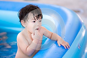 Cute boy poked his hand in his mouth. Baby play in the rubber pool in summer. Child wet aged 1-2 years old
