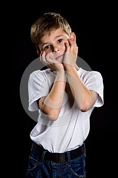 Cute boy portrait with palms holding on the cheeks on the black background