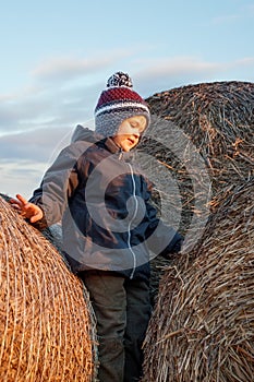 A cute boy poses on top of a pile of straw bales, sunset lights, a background of blue sky