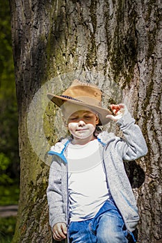 Cute boy posing in a cowboy hat in the woods by a tree. The sun`s rays envelop the space. Interaction history for the book. Space