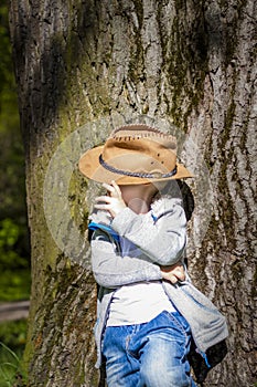 Cute boy posing in a cowboy hat in the woods by a tree. The sun`s rays envelop the space. Interaction history for the book. Space