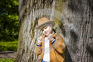 Cute boy posing in a cowboy hat in the woods by a tree. The sun`s rays envelop the space. Interaction history for the book. Space