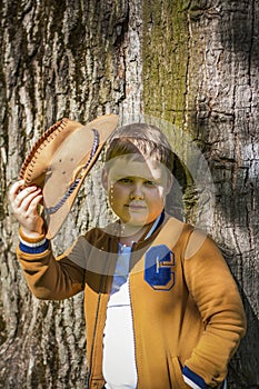 Cute boy posing in a cowboy hat in the woods by a tree. The sun`s rays envelop the space. Interaction history for the book. Space