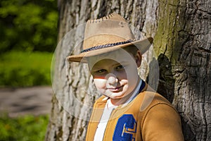 Cute boy posing in a cowboy hat in the woods by a tree. The sun`s rays envelop the space. Interaction history for the book. Space