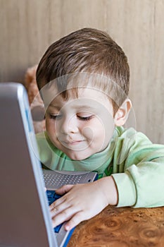 Cute boy is pushing laptops keyboard and he is looking at the screen.