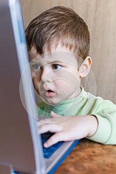 Cute boy is pushing laptops keyboard and he is looking at the screen.