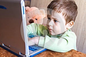 Cute boy is pushing laptops keyboard and he is looking at the screen.