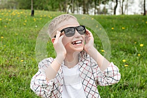 Cute boy put on colorblind sunglasses and laughs. Snow-white teeth in a boy in sunglasses