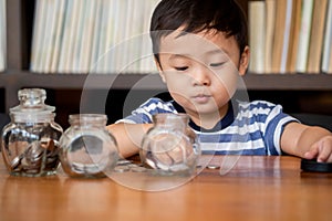 Cute boy putting money coins in glass,saving money concept