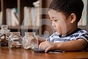 Cute boy putting money coins in glass,saving money concept