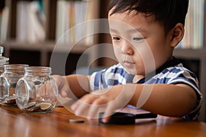 Cute boy putting money coins in glass,saving money concept