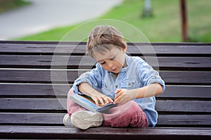 Cute boy, read a book in the park, sitting on bench, summertime