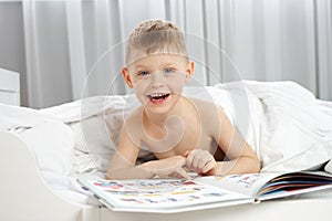 Cute boy reading a book in a white baby bed